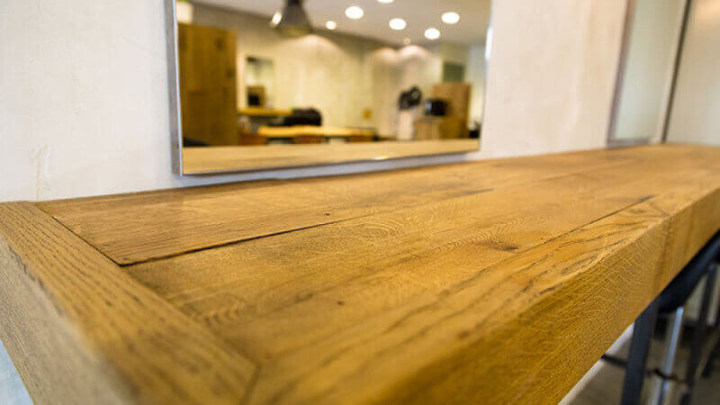 A wood floating shelf in a barbershop with a mirror above it.