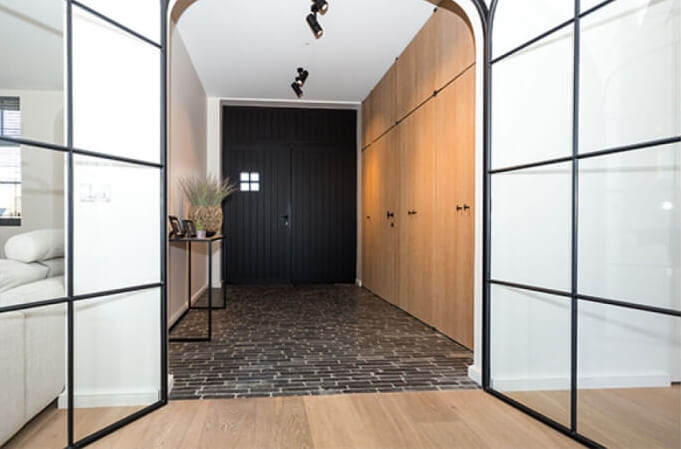 Living room with wood flooring opening into a tiled hallway with glass doors.