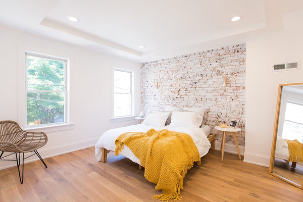 Bedroom with hardwood flooring, bed and brick accent wall.
