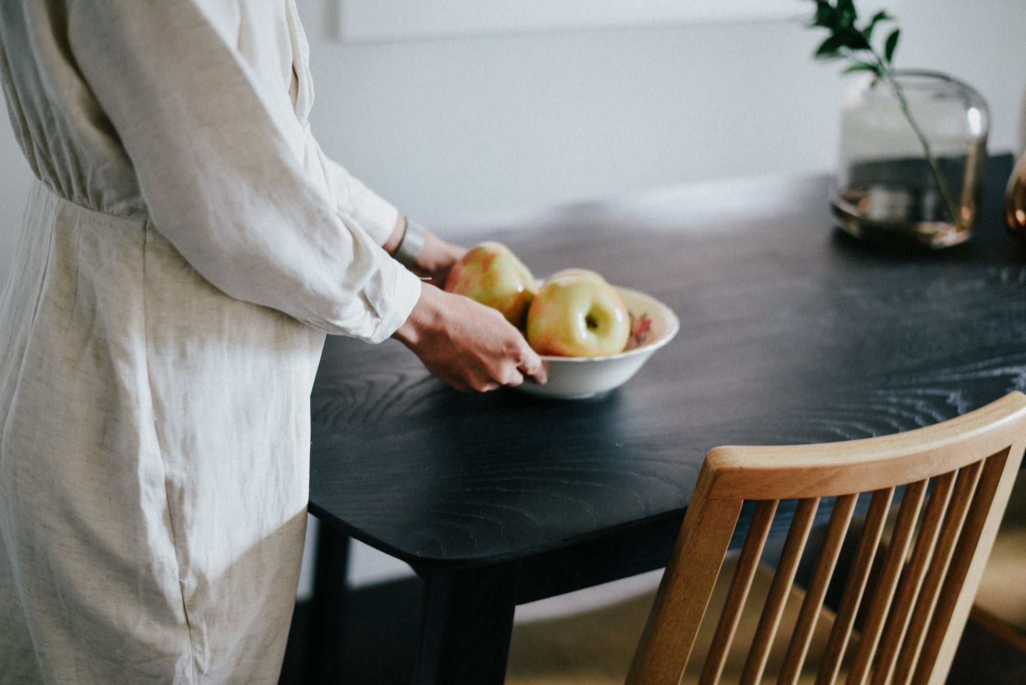 A woman sets down a bowl of fruit on a black solid ash dining table.