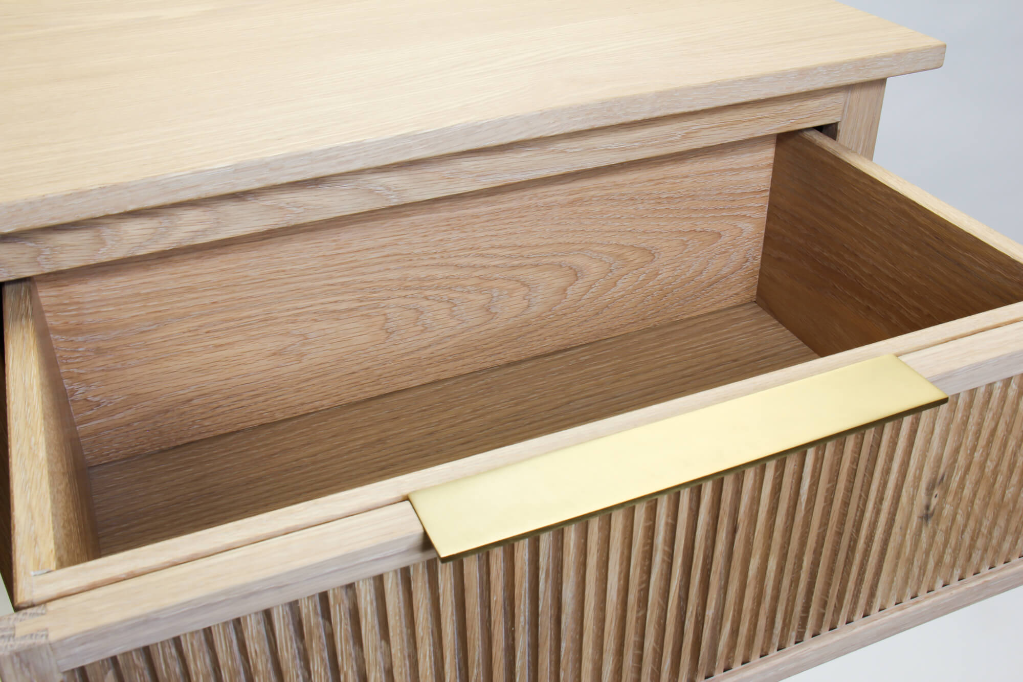 An open dresser drawer with a reeded drawer front and brass pull is pictured. It is finished with Rubio Monocoat hardwaxoil.