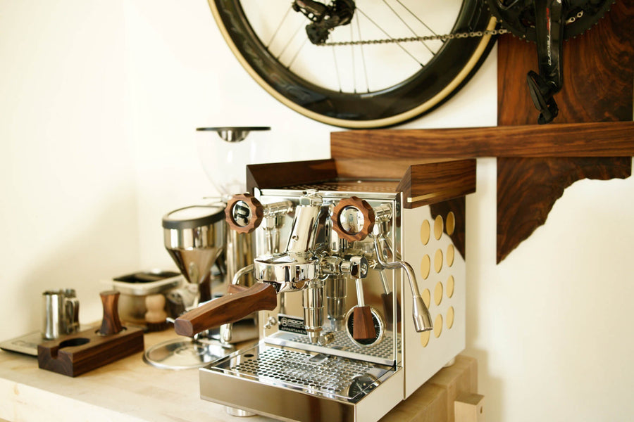 Rocket Apartamento espresso machine with walnut accents. Various espresso accessories sit beside it in an organizer made from walnut.