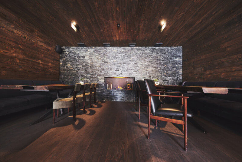A moody restaurant dining room with wood floors, walls, and ceiling with a masonry accent wall.