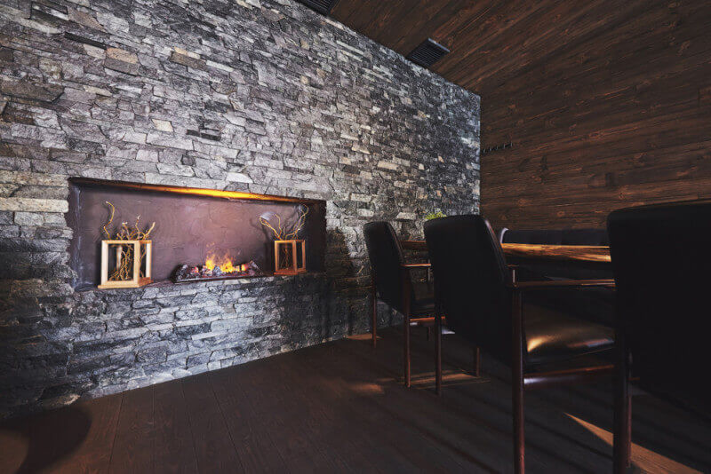 A moody restaurant dining room with wood floors, walls, and ceiling with a stone accent wall.