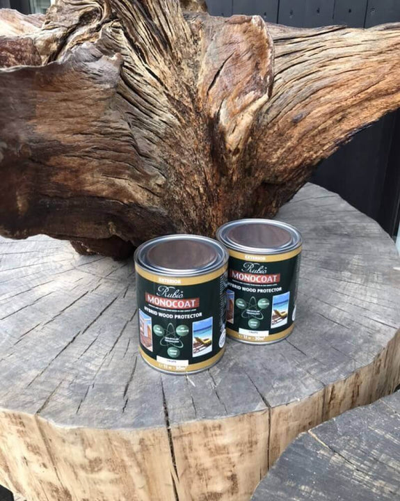 Rubio Monocoat Hybrid Wood Protector cans sitting on a tree stump outside.