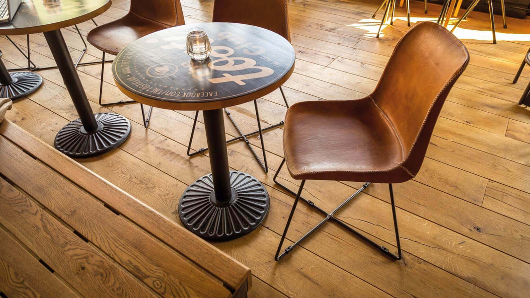 A small table with a leather chair at it on an aged oak floor.