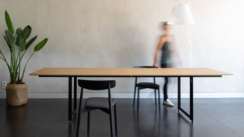 Woman walks behind oak wood table finished with Rubio Monocoat hardwax oil.