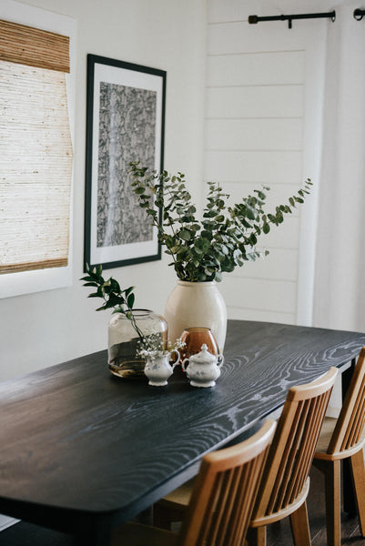 Several decorative accents sit on top of a black stained ash table with wood-toned chairs.