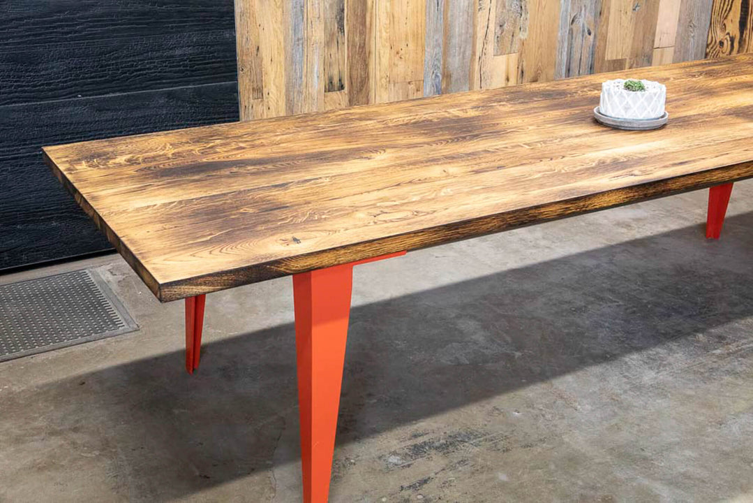 Orange metal legs are on a charred white oak dining table finished with Rubio Monocoat Oil Plus 2C hardwax oil wood stain and finish.