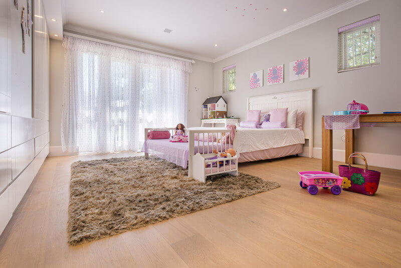 Young girls room with wide plank wood flooring in it.