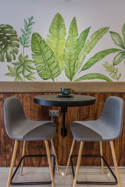 A commercial, 2 seat coffee table with chairs against wooden paneling on the bottom half of the wall and artwork on the top half of the wall.