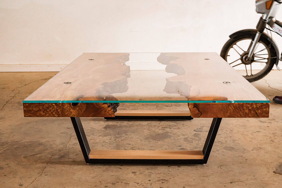 Burled maple coffee table with a glass top; a motorcycle wheel is seen in the background.