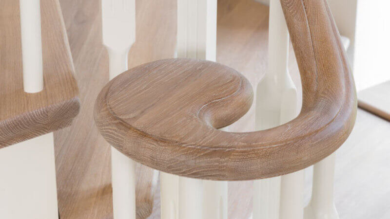 A curved handrail for stairs that is finished with a natural, plant-based wood finish.