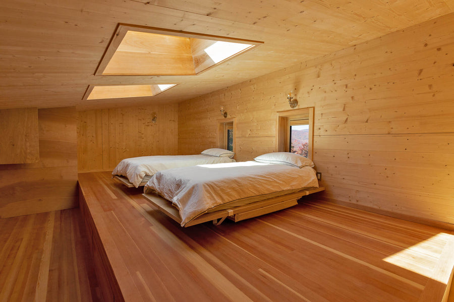 A guest bedroom with wood flooring and wood wall paneling finished with Rubio Monocoat hardwax oil products. This room also features two sky lights.