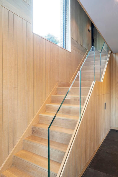 Wood staircase with wood paneling on the side and a glass banister and handrail.