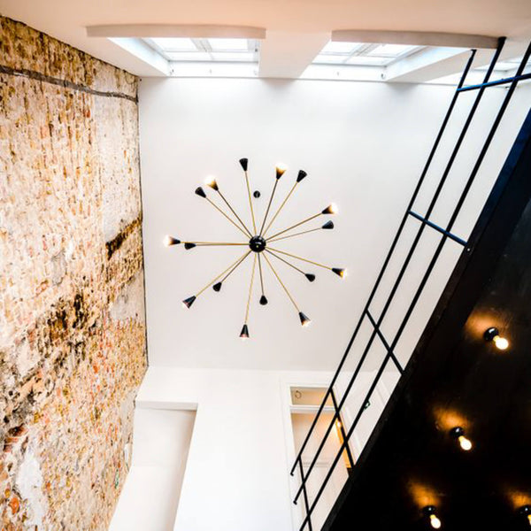 Looking up, a modern light fixture hangs from the ceiling and there is a brick wall to the right and a black wooden overhand to the left with railing.