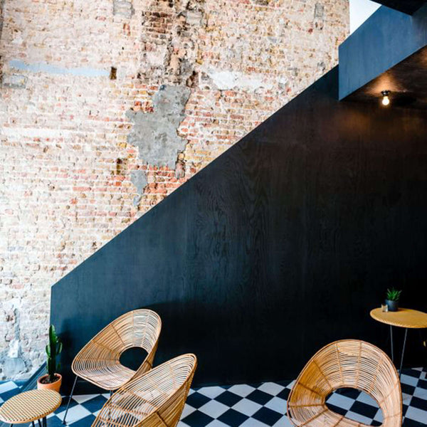 A Rubio Monocoat stained black wood wall is in the background and three wicker chairs are also pictured on top of a black and white checkered floor.
