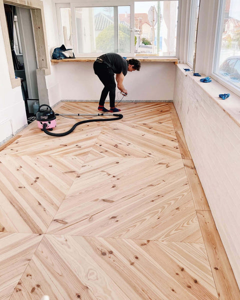 A man is finishing up the final details on a chevron patterned floor prior to applying Rubio Monocoat, a hardwax oil wood finish.