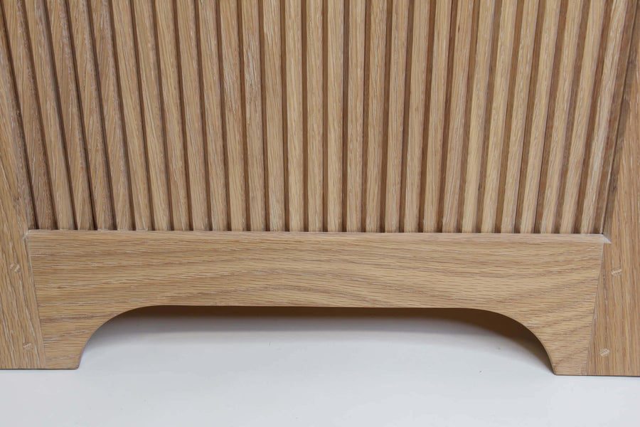 The side view of the bottom of the white oak storage dresser. Beautiful reeding adorns the side and features a gently curved base.