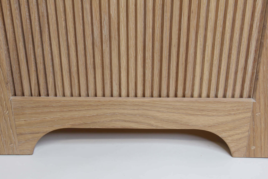 The side view of the bottom of the white oak storage dresser. Beautiful reeding adorns the side and features a gently curved base.