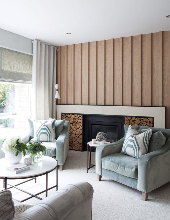 Fluted white oak accent wall finished with Rubio Monocoat Oil Plus 2C Natural, framing a black stone fireplace with built-in log storage in a sage-green living room.