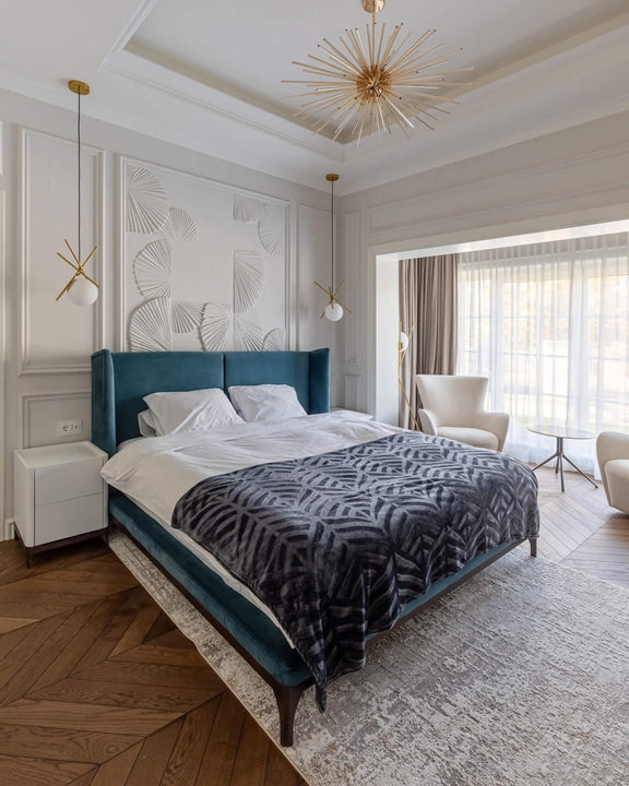 Luxury bedroom featuring double-layer white oak chevron parquet finished with Rubio Monocoat Oil Plus 2C hardwax oil in a custom shade, paired with a teal velvet wingback bed, white sculptural wall relief, and gold sputnik chandelier.