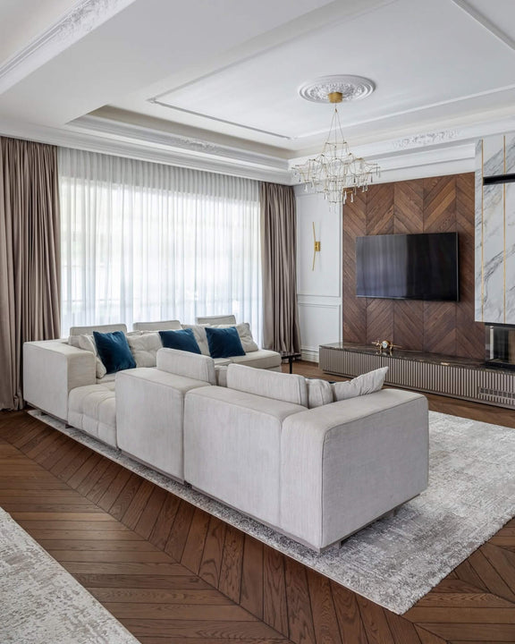 Bright living room with white oak chevron parquet finished in Rubio Monocoat Oil Plus 2C hardwax oil, a cream sectional sofa with teal velvet pillows, and a matching chevron wood-paneled TV wall with marble and gold accents.