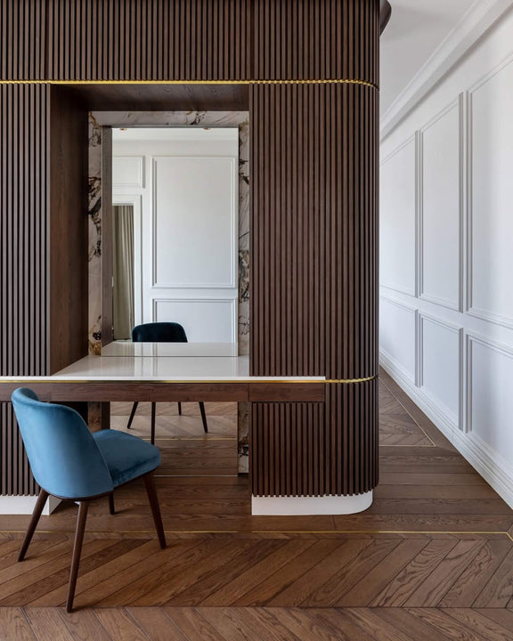 Desk area with Rubio Monocoat Oil Plus 2C-finished white oak chevron parquet flooring, visible brass border inlays, dark walnut fluted wood slat walls, and a teal velvet  chair.