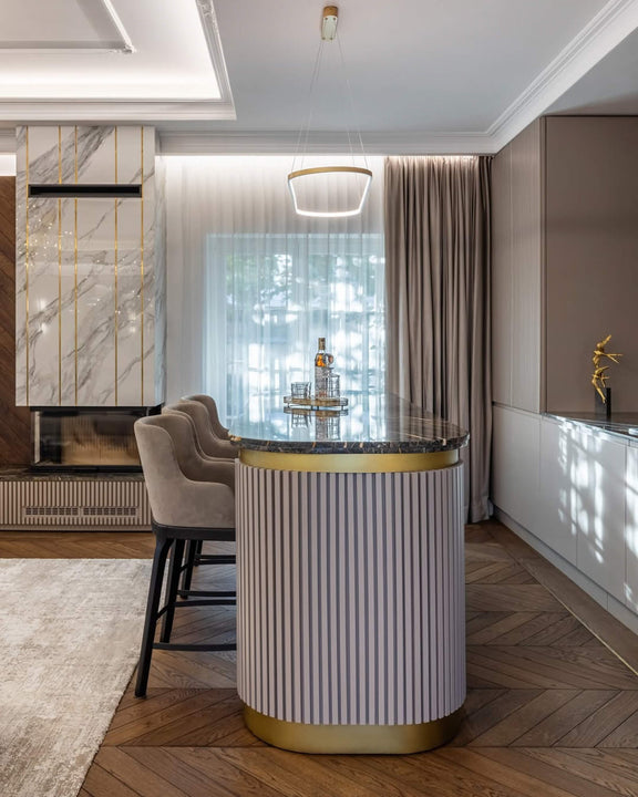 Home bar with Rubio Monocoat Oil Plus 2C-finished white oak chevron parquet flooring, a cylindrical fluted bar island with brass band and dark marble top, and a dramatic marble fireplace wall with vertical gold inlays.