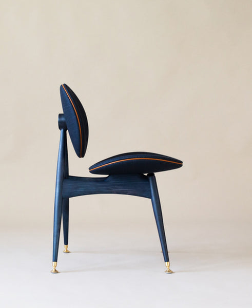 The side view of a modern dining chair featuring blue wood finished with a hardwax oil, leather and brass accents and a coordinating blue fabric.