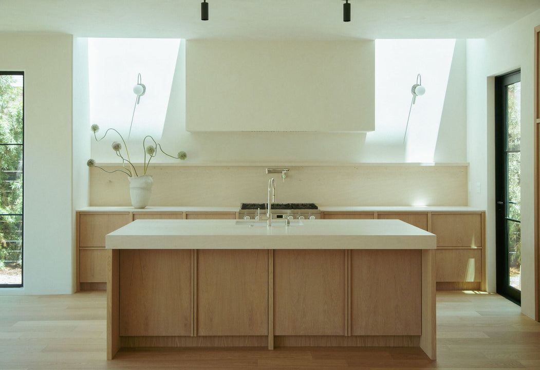 Symmetrical white oak kitchen with Rubio Monocoat Oil Plus 2C Natural finish, centered island, stainless range, and dual skylights flanking the hood.