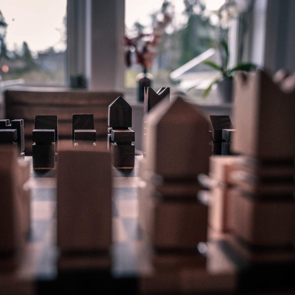Maple chess pieces are out of focus in the foreground. In the background of the photos, handmade walnut chess pieces are pictured.