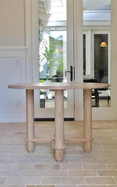 Round white oak table with four rounded legs and dimensional details.