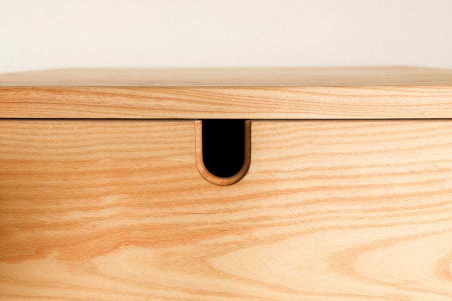 A tight shot of an ash nightstand with an integrated finger pull.
