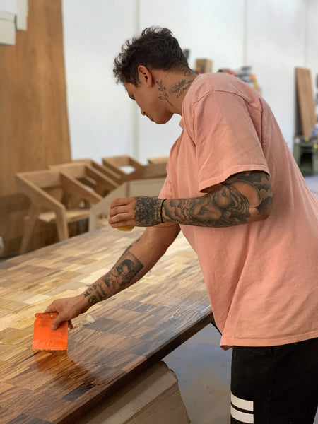 A man is spreading a hardwax oil wood finish onto a dining table top.