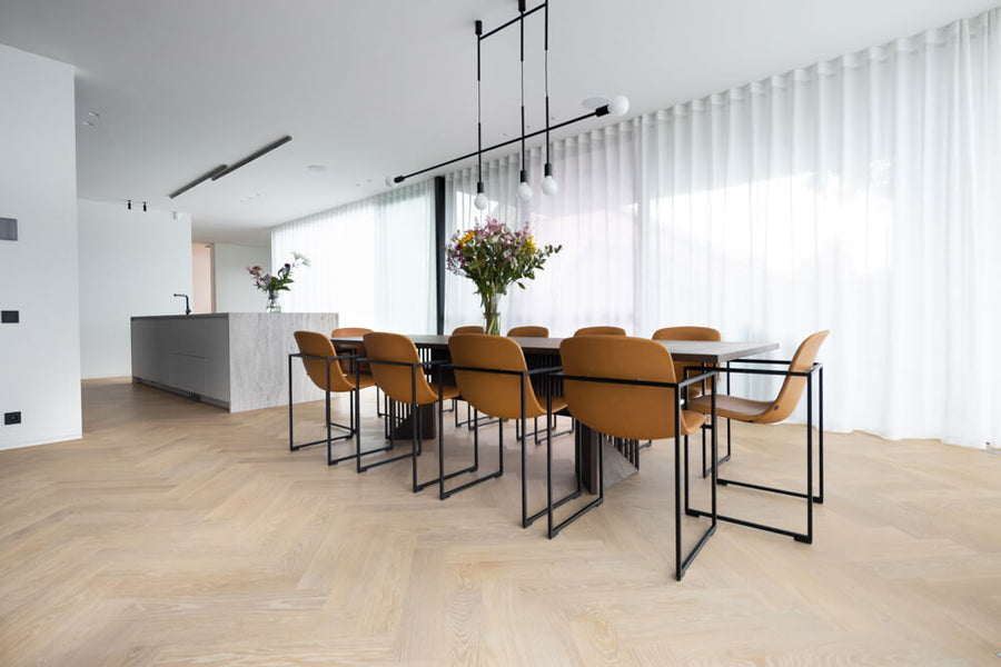 A natural colored herringbone white oak floor in a dining area. The space features a long dining table with seating for 10 people.