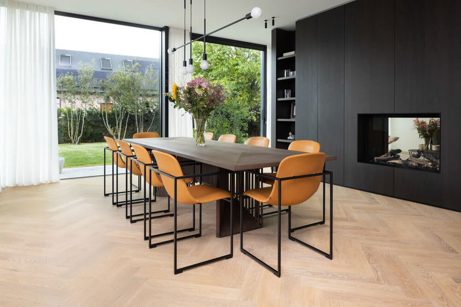 A dining area with light, natural colored flooring finished with Oil Plus 2C hardwax oil. A large, dark dining table and fireplace built-in is seen in the background.
