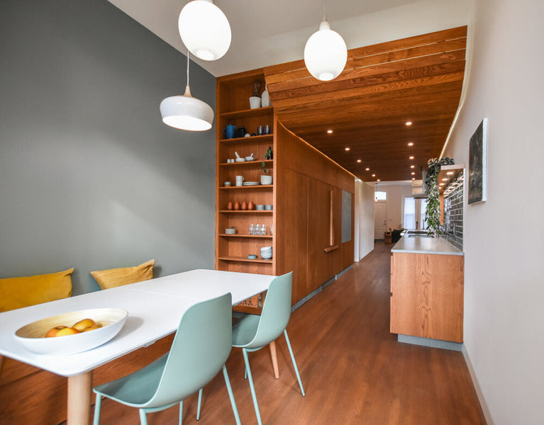 A dining area with a built-in bench looking into a galley kitchen with wood cabinetry and shelving.