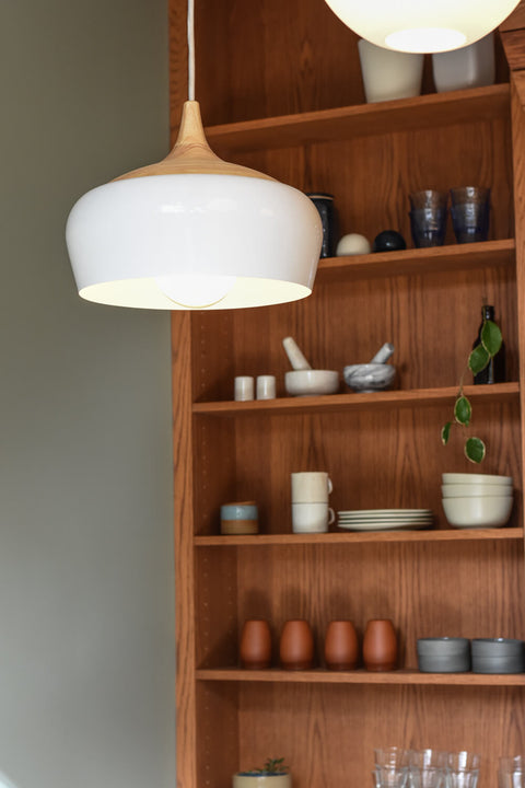 A white, modern light fixture with wood shelving in the background adorned with a variety of decor elements.