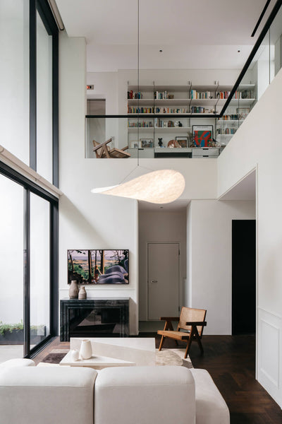 A living room with a dark wood floor and white sofa being overlooked by a balcony with a library area.