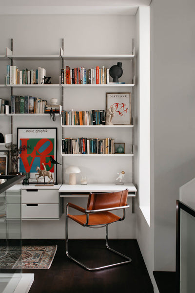 A mid-century modern inspired chair sits adjacent to a bookshelf with a built in desk and drawers.