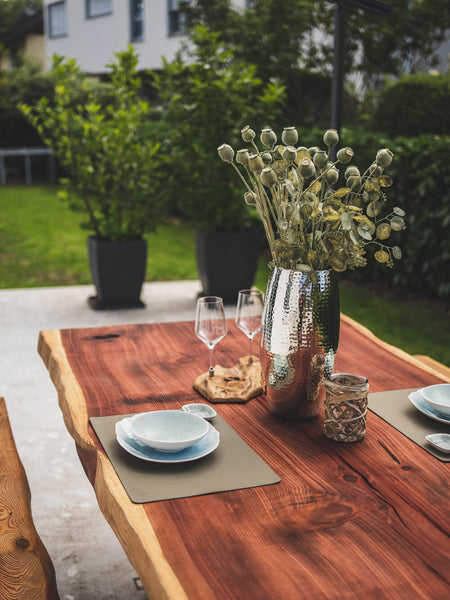 Two place settings and a vase with flowers sit atop a redwood dining table finished with Hybrid Wood Protector.