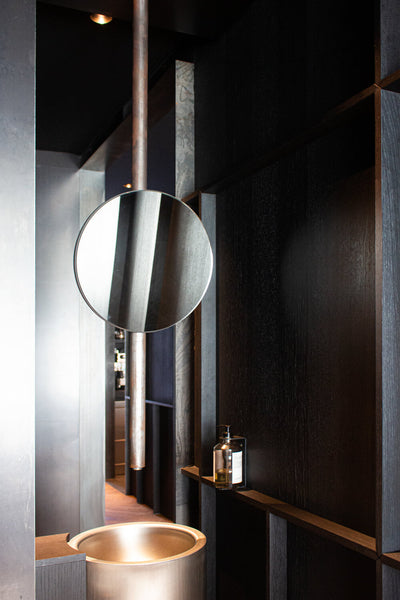 A mirror hangs on a wall with opaque black millwork in the background made from oak wood.