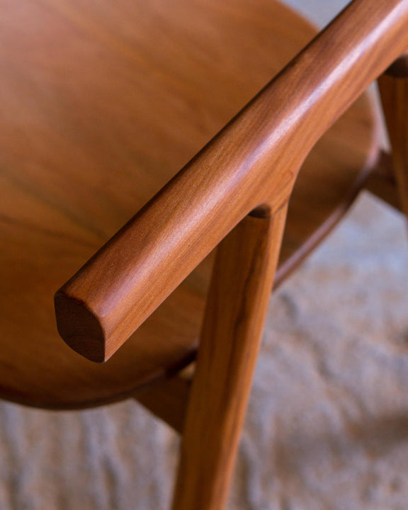 Close-up of the rounded armrest tip of a walnut chair, showcasing the hand-shaped end grain.