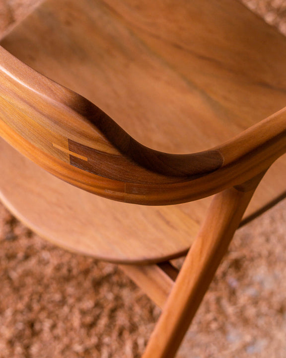 Overhead detail of a walnut chair's curved back rail with exposed butterfly joint inlays, shot above a bed of wood shavings.