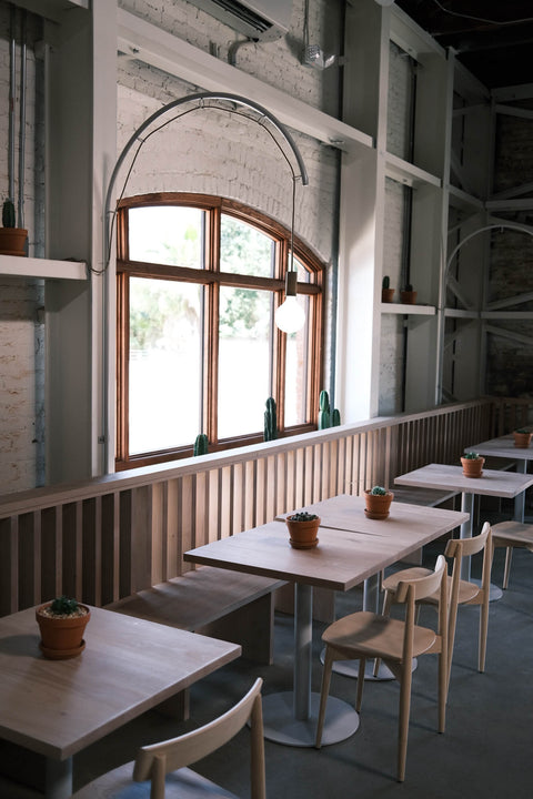 Many tables and chairs fixed in front of a window in a restaurant.