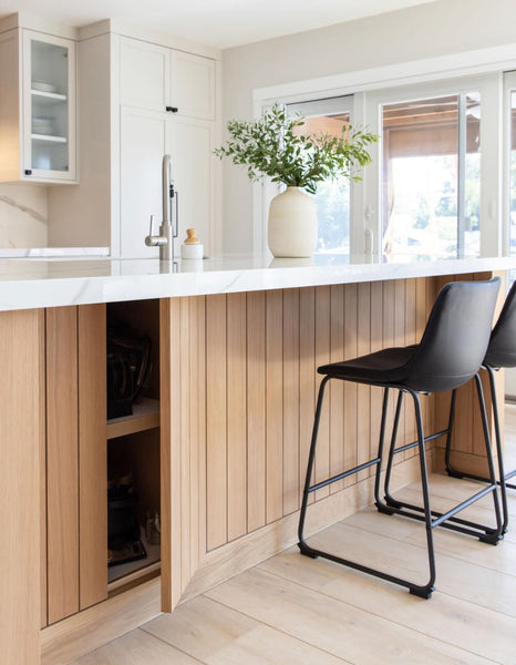A white oak island with vertical paneling revealing hidden cabinetry space.