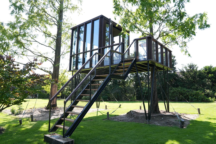 A wooden tree house with a large staircase made from Afzelia wood and finished using a strong exterior wood finish by Rubio Monocoat called DuroGrit.
