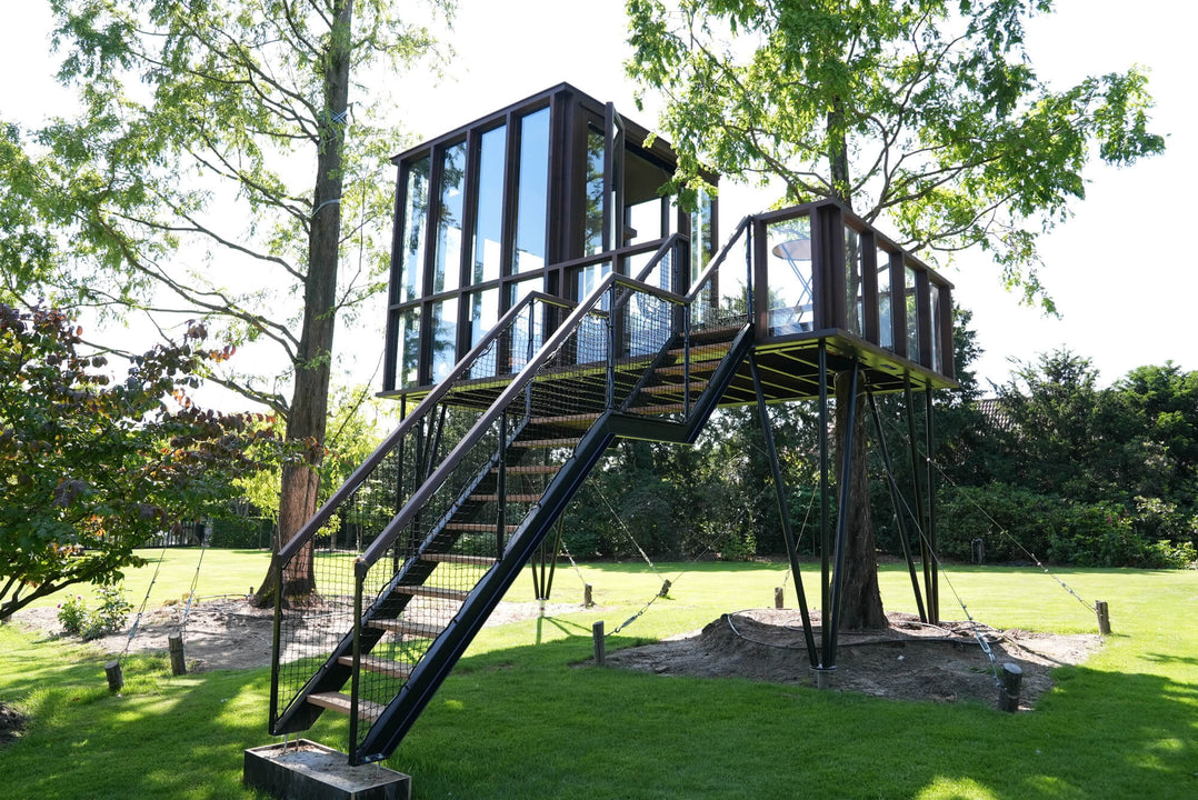 A wooden tree house with a large staircase made from Afzelia wood and finished using a strong exterior wood finish by Rubio Monocoat called DuroGrit.