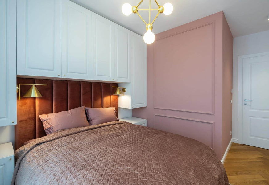 A rose pink bedroom with white cabinets and herringbone hardwood flooring.